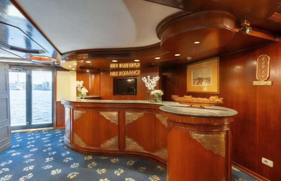 Curved, polished wood reception desk with marble countertops and traditional Egyptian decor in the ship's lobby.