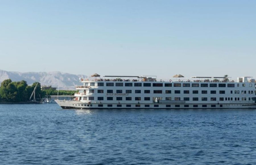 A wide, white, multi-deck river cruise ship named "Nile Romance" sailing on the blue river under a clear sky.