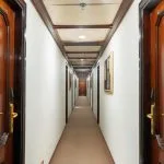Ship corridor with white walls, a beige carpet, and traditional dark wood cabin doors with brass handles.