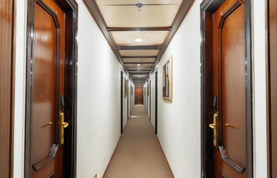 Ship corridor with white walls, a beige carpet, and traditional dark wood cabin doors with brass handles.