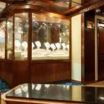 Interior view of a cruise ship jewelry shop with a large, illuminated wooden display case showing necklaces and pendants.