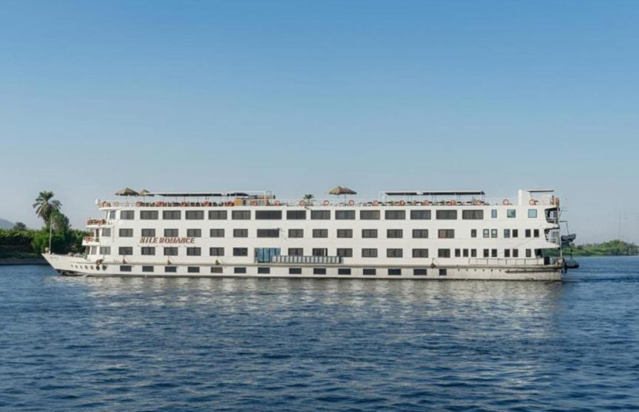 A wide, white, multi-deck river cruise ship named "Nile Romance" sailing on the blue river under a clear sky.