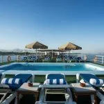 Swimming pool on a cruise ship sundeck with sun umbrellas, lounge chairs, and a panoramic view of the Nile.