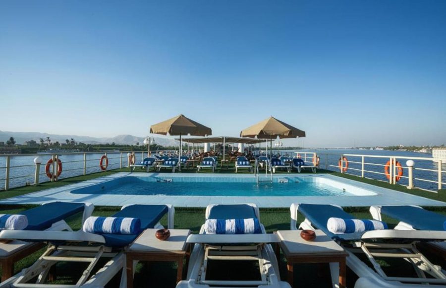 Swimming pool on a cruise ship sundeck with sun umbrellas, lounge chairs, and a panoramic view of the Nile.