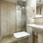 Small, cruise ship bathroom with a white pedestal sink, toilet, and a glass-enclosed shower.