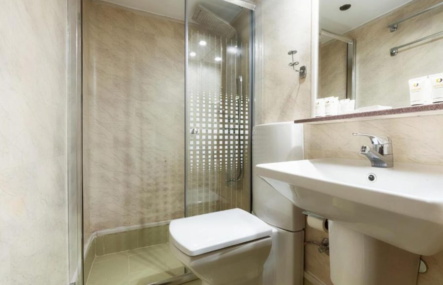 Small, cruise ship bathroom with a white pedestal sink, toilet, and a glass-enclosed shower.