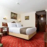 Traditional style single cabin on a Nile cruise with a large bed, red patterned carpet, and dark wood furniture.