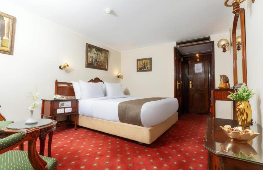 Traditional style single cabin on a Nile cruise with a large bed, red patterned carpet, and dark wood furniture.
