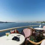 Rattan table and chairs on a cruise ship sundeck with binoculars and cocktails, overlooking the wide Nile River.