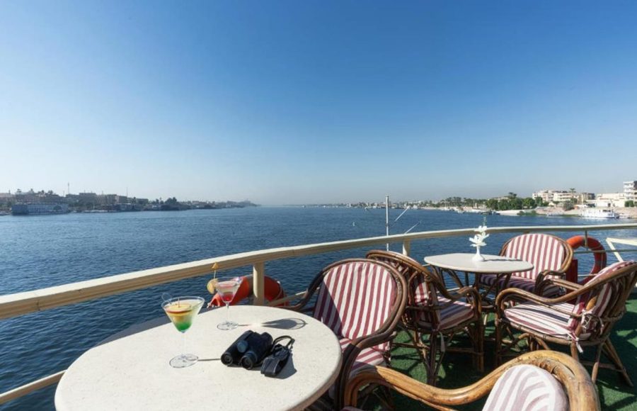 Rattan table and chairs on a cruise ship sundeck with binoculars and cocktails, overlooking the wide Nile River.