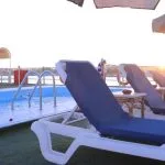 Rows of white outdoor tables and chairs under a brown canopy on the cruise ship's sun deck, overlooking the Nile River.