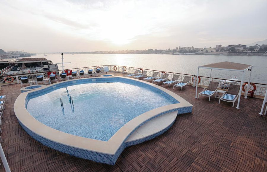 Heart-shaped outdoor pool on a wooden cruise ship deck at sunset.