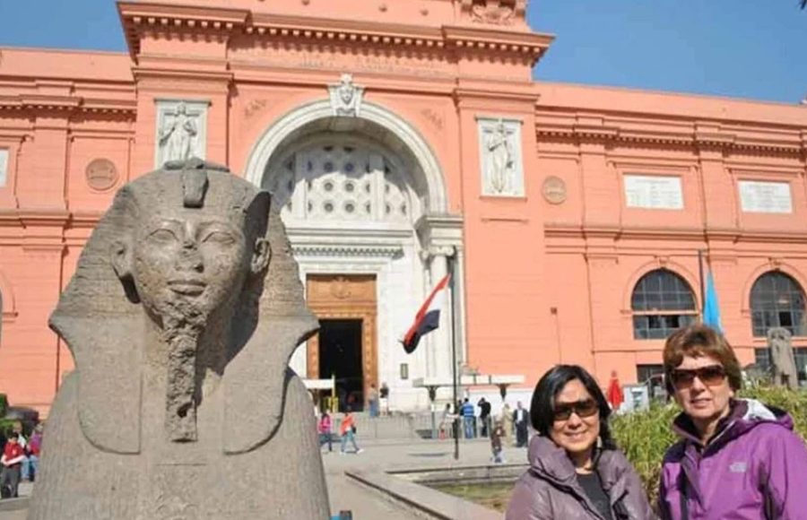 Tourists stand near a pharaonic statue in front of the pink Egyptian Museum, a stop on your pyramids and museum day trip