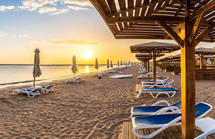 A sandy beach at the Red Sea lined with umbrellas and lounge chairs.