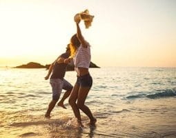 Two people splashing and dancing in the shallow ocean water at sunset, a joyful moment on an overland trip in Egypt.