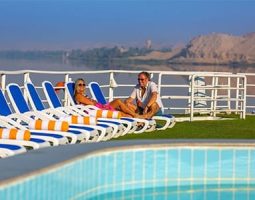 Two tourists relaxing on sun loungers by a pool on the deck of a standard Nile cruise ship.