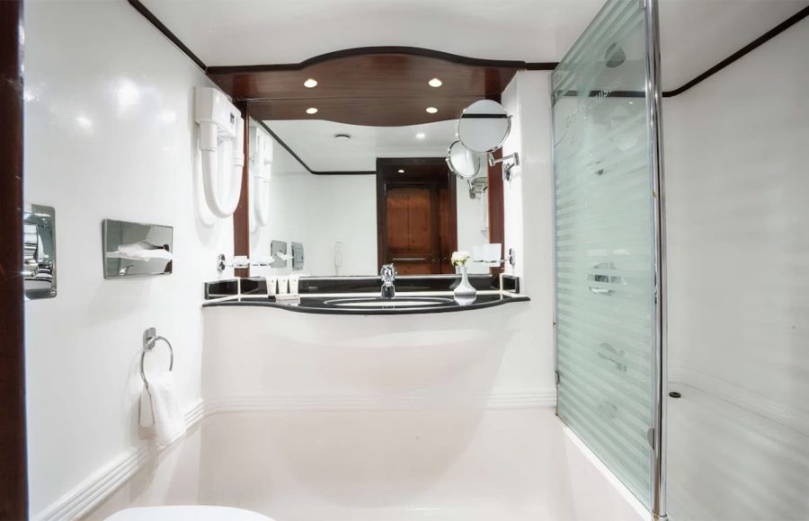 Modern, white suite bathroom with glass shower and wooden mirror frame on a cruise ship.