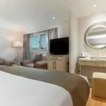 Interior of a Nile cruise ship cabin featuring a bed, seating area, dressing table, and window.