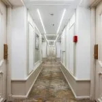 Long, symmetrical hallway of a cruise ship lined with light-colored cabin doors and illuminated by strip lighting.