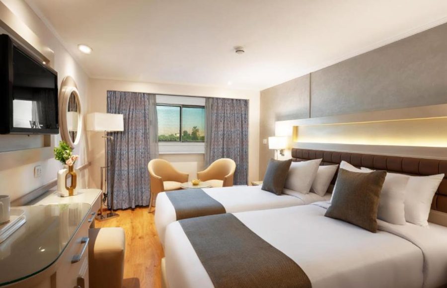 Interior of a Nile cruise ship cabin with two twin beds, a small seating area, and modern furniture.