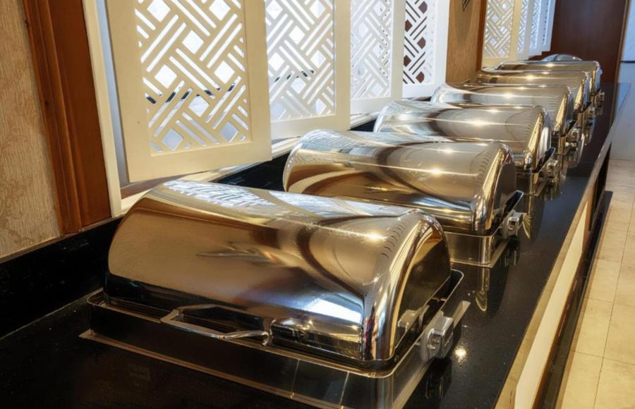 A line of stainless steel chafing dishes on a buffet counter, ready to serve hot food.