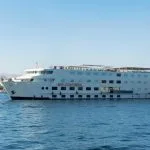 A large, white, multi-deck Nile cruise ship named "M/S Sun Times" sailing on the blue river under a clear sky.