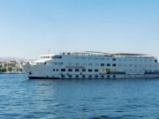 A large, white, multi-deck Nile cruise ship named "M/S Sun Times" sailing on the blue river under a clear sky.