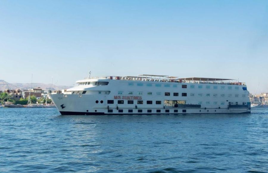 A large, white, multi-deck Nile cruise ship named "M/S Sun Times" sailing on the blue river under a clear sky.