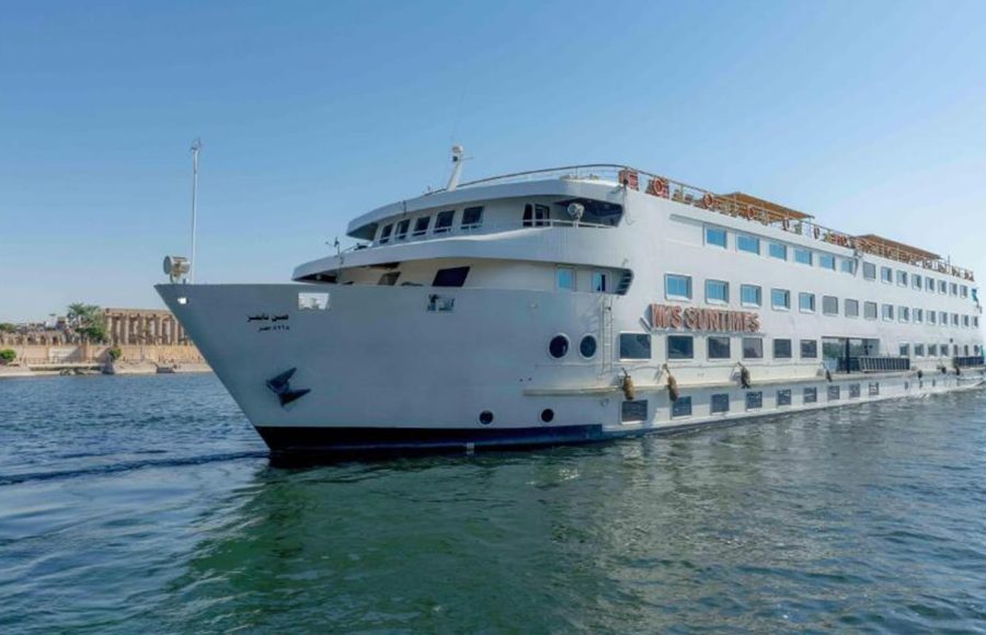 The M/S Sun Times cruise ship sailing close to the river bank with the ruins of an ancient Egyptian temple visible behind it.