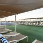 Interior view of a bright, modern cruise ship cabin with a large bed, seating area, and vanity.
