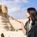 A young woman blowing a kiss towards the camera with the ancient Great Sphinx of Giza and a pyramid in her 6 days Cairo and Hurghada Holiday Package.