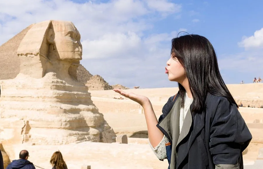A young woman blowing a kiss towards the camera with the ancient Great Sphinx of Giza and a pyramid in her 6 days Cairo and Hurghada Holiday Package.