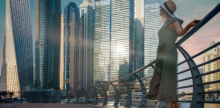 tourist woman in fashionable summer dress and hat enjoying Dubai marina skyline at sunset
