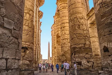 Tourists walking between the massive columns at Karnak Temple in Luxor, a stop on your Lake Nasser and Nile Cruise Itinerary.